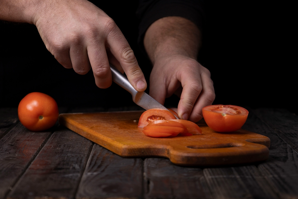 A close up of some quality knives cutting a tomato on a cutting board